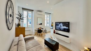 A modern living room with a large TV, a sofa, a coffee table, and a dining area with chairs and a table.
