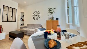 A modern living room with a sofa, a dining table with a croissant, a clock, and a plant.