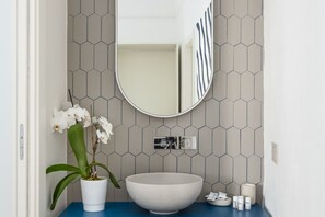 Une salle de bain avec un lavabo blanc, un miroir et une orchidée en pot.