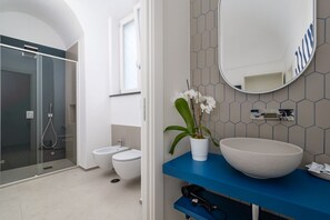 Une salle de bain moderne avec une douche à parois de verre, des toilettes blanches, un lavabo avec un grand bac et une orchidée en pot.