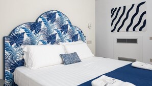 Une chambre d’hôtel avec un lit, du linge de lit blanc, une tête de lit bleue ornée d’un motif de feuilles, une couvre-lit bleue et un mur décoré de rayures zébrées.