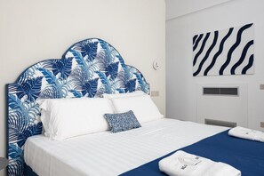 Ein Hotelzimmer mit einem Bett, weißer Bettwäsche, einem blauen Kopfteil mit Blätermotiv und einer blauen Tagesdecke. An der Wand ist ein Zeprazebramuster zu sehen.