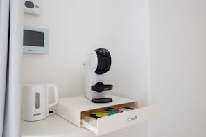 Une machine à café, une horloge numérique et un tiroir contenant des dosettes de café.
