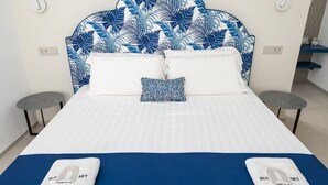 Habitación de hotel con cama, dos mesitas de noche, cabecero con diseño de hojas y decoración azul y blanca.
