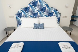Ein Hotelzimmer mit einem Bett, zwei Nachttischen, einem Blattmuster am Kopfteil und einer blauen und weißen Farbgestaltung.