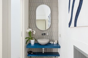 Une salle de bain avec un lavabo blanc, une étagère bleue, un miroir et une orchidée en pot.