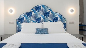 Una habitación de hotel con una cama, cabecera con diseño de hojas, dos lámparas de noche y una mesita.