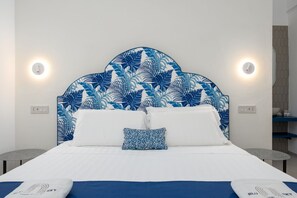 Ein Hotelzimmer mit einem Bett, einem Blattmuster-Kopfschild, zwei Nachttischlampen und einem kleinen Tisch.