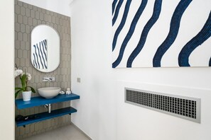 Un baño con lavamanos blanco, repisas azules, un espejo y un respiradero.