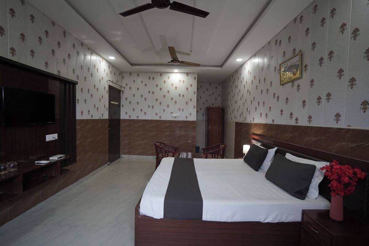 Une chambre d’hôtel comprenant un lit, une télévision, un ventilateur de plafond, une armoire en bois et une petite table avec une chaise.