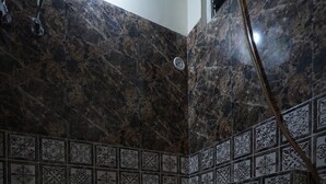 A bathroom with dark marble walls, patterned tiles, a white sink, and a shower. - NOVA RESORTS (Raebareli)