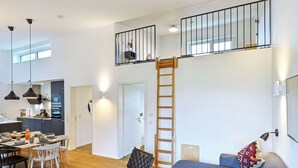 Een ruime woonkamer met een eettafel, stoelen, een bank en een ladder naar een slaapverdieping.
