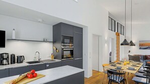Une cuisine moderne dotée d’un îlot central, d’appareils électroménagers intégrés et d’un coin repas avec une table et des chaises en bois.