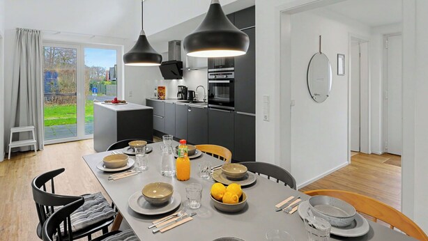 Une cuisine moderne avec un coin repas, de grandes fenêtres et une vue sur l’extérieur.