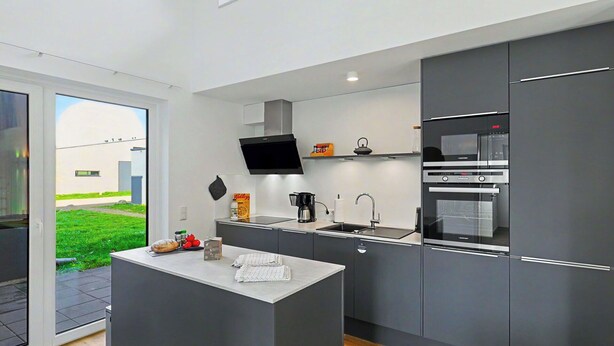 A modern kitchen with a central island, built-in appliances, and a view of a green outdoor area. - Wonderful private villa for 8 people with WIFI, TV and terrace (Diepholz)