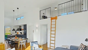 A modern interior with a dining area, a living room with a sofa and coffee table, a kitchen with a balcony, and a wooden ladder. - Wonderful private villa for 8 people with WIFI, TV and terrace (Diepholz)