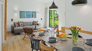 Moderni olohuone, jossa on sohva, ruokapöytä, tuoleja ja taideteoksia seinällä.