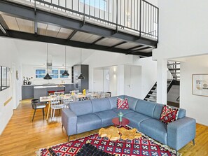 Una sala de estar moderna con un sofá seccional azul, una zona de comedor y una cocina al fondo.