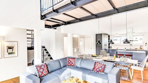 Ein modernes Wohnzimmer mit einer grauen Eckcouch, einem Essbereich mit Holztisch und einer Küche im Hintergrund.