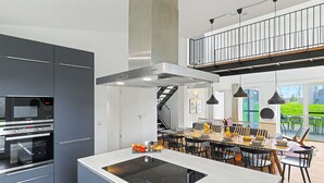 Eine moderne Küche mit Einbauofen, einer zentralen Kochinsel mit Induktionskochfeld und einem Essbereich mit großem Tisch und Stühlen.