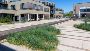 Eine moderne Stadtstraße mit mehrstöckigen Gebäuden, Außenbereichen zum Verweilen und einem Fußgängerweg.