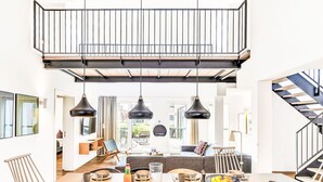 Ein moderner Essbereich mit hoher Decke, schwarzen Pendelleuchten und einer Treppe, die zu einer oberen Ebene führt.