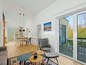 Een moderne woonkamer met een eethoek, een grijze fauteuil en een grote schuifpui die uitkomt op een terras.