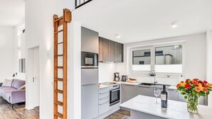 Cozinha moderna com micro-ondas embutido, forno e cafeteira. Uma escada de madeira leva a um mezanino.