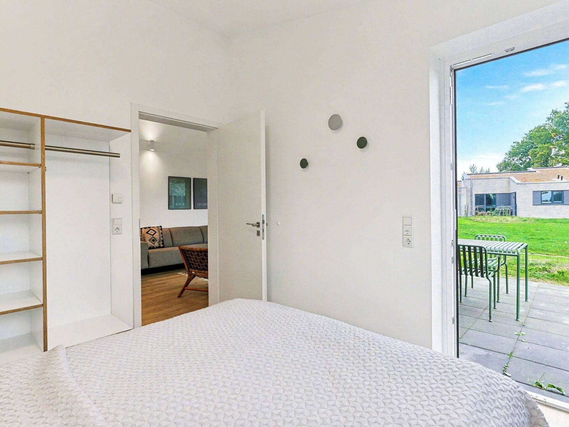 A modern bedroom with a large bed, a wooden wardrobe, and a sliding glass door leading to a balcony with outdoor furniture.