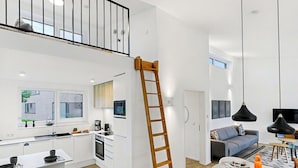 Een moderne keuken met witte kastjes, een houten trapje en een eethoek met een ronde tafel en zwarte stoelen.