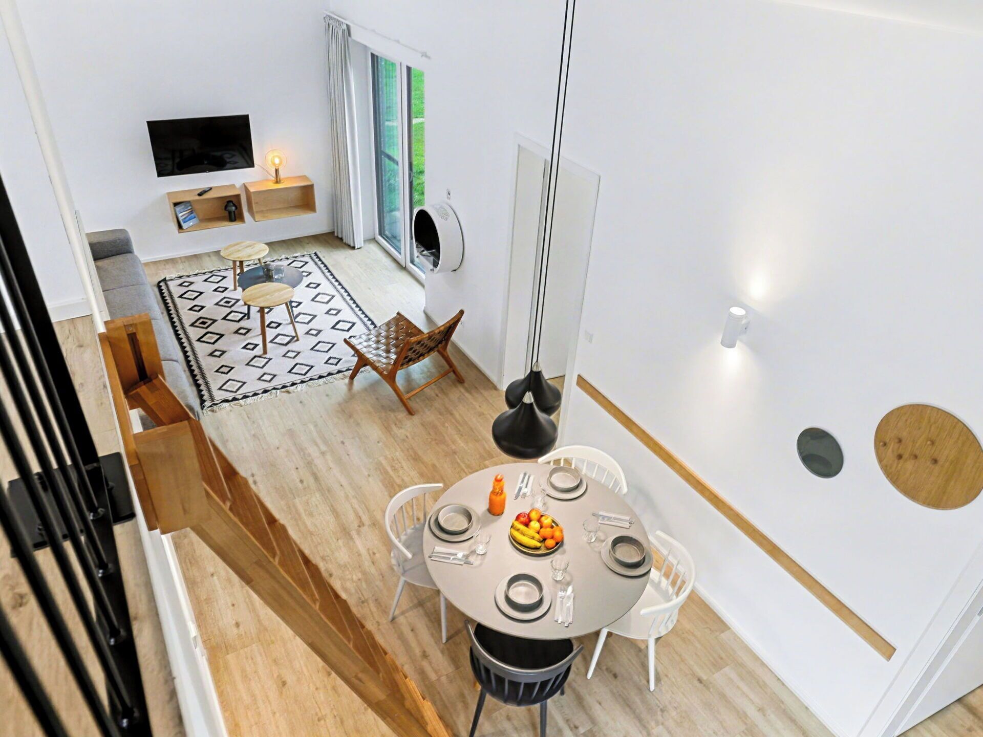 Et moderne spiseområde med et rundt bord, hvide stole og en skål med frugt.