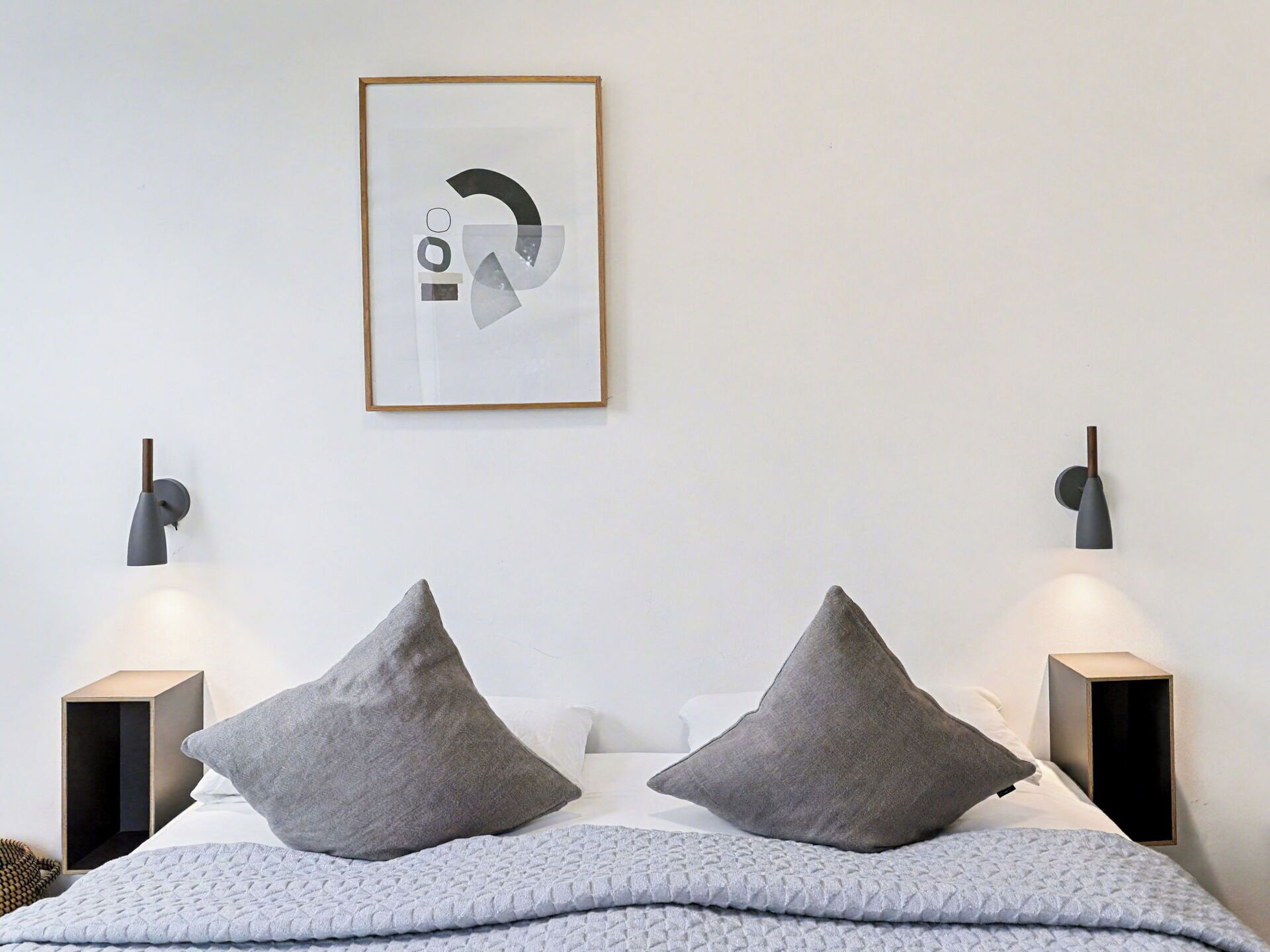 A modern bedroom with a bed, two bedside lamps, and a framed abstract artwork on the wall.