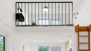 Een moderne keuken met een centraal eiland, twee krukken, een houten trap en een raam met uitzicht op een tuin.