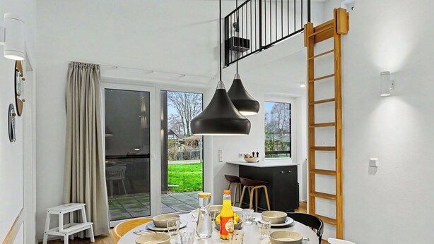 A dining area with a round table set for four, a kitchen in the background, and a view of the outdoors through a sliding glass door. - Stunning private villa for 6 guests with WIFI, TV and terrace (Diepholz)