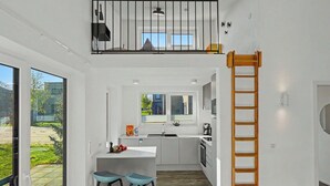 Cozinha moderna com ilha central, banquetas, escada de madeira e vista para o exterior.