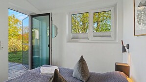 Quarto com cama, duas janelas, uma porta e uma mesa de cabeceira.