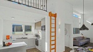 Uma cozinha moderna com uma ilha central, um espaço de jantar com mesa posta para quatro pessoas e uma sala de estar com sofá.