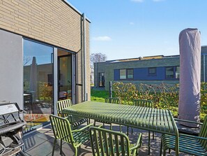 En terrasse med et bord og stole, grill og en bygning med murstensfacade og store vinduer.
