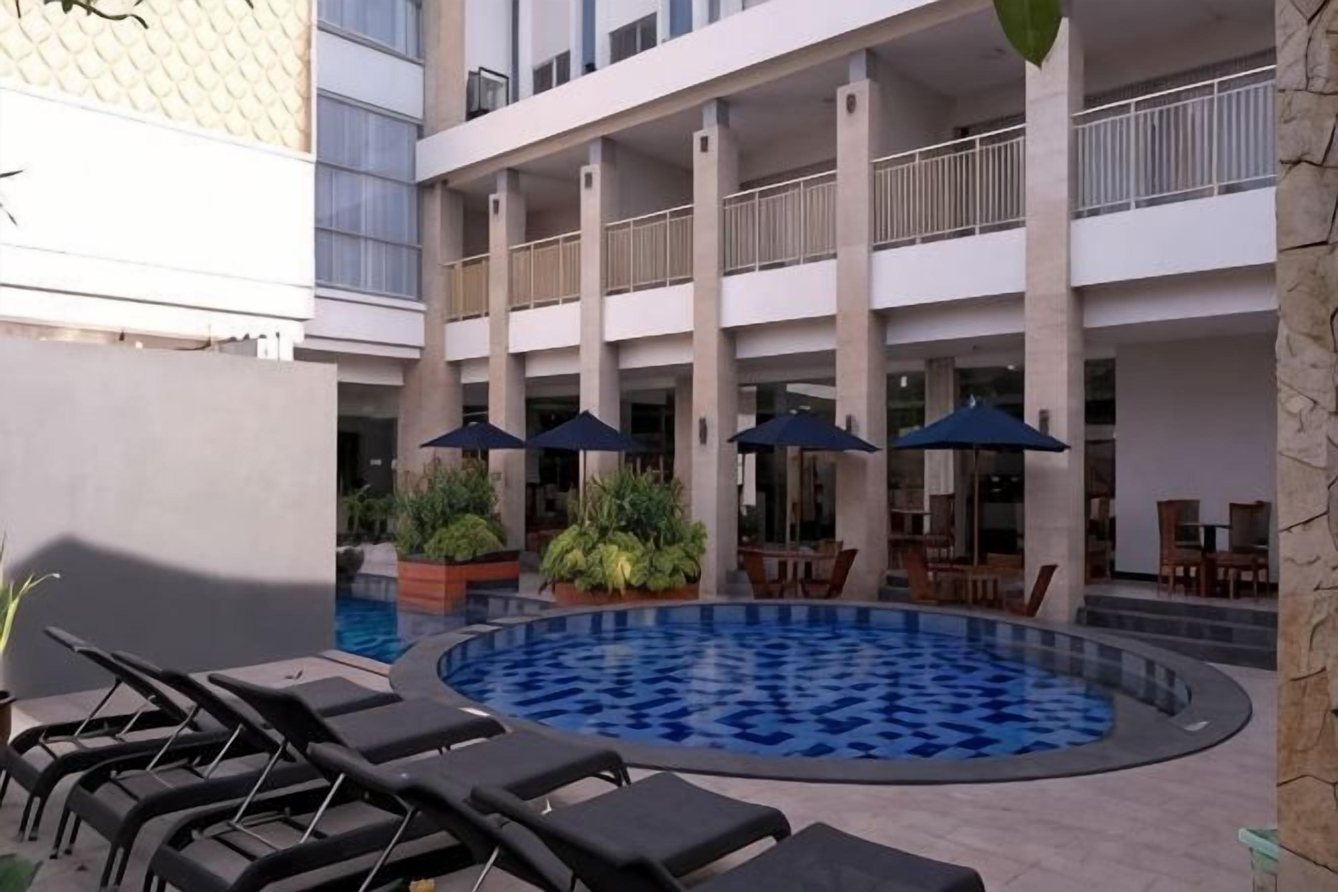 Zona de piscina con sillones de descanso, sombrillas y comedor con mesas y sillas.