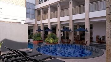 Zona de piscina con sillones de descanso, sombrillas y comedor con mesas y sillas.