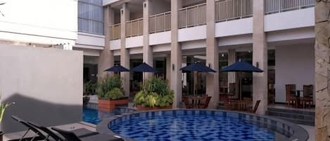 A pool area with lounge chairs, umbrellas, and a dining area with tables and chairs.