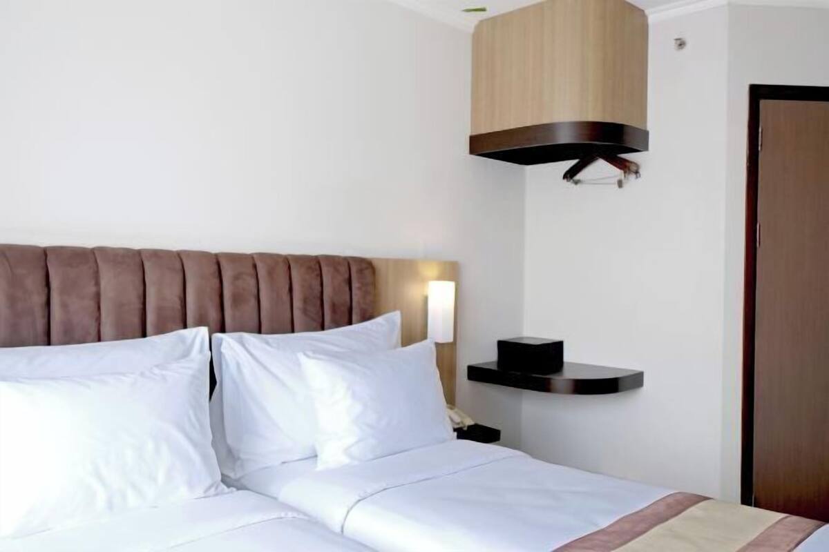 Une chambre d’hôtel avec un lit, une tête de lit, une table de chevet, une lampe et une porte.