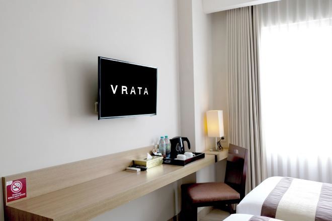 Habitación de hotel con televisión en la pared, escritorio con cafetera, una silla y cama con colcha a rayas.