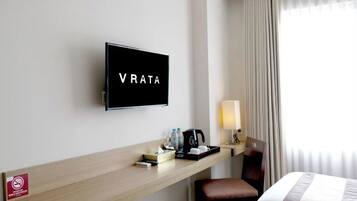 Habitación de hotel con televisión en la pared, escritorio con cafetera, una silla y cama con colcha a rayas.