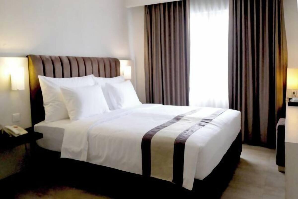 Une chambre d’hôtel avec un lit, des tables de chevet, une commode, une lampe et des rideaux.