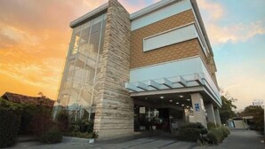 A modern building with a glass facade and a stone base, featuring a covered entrance area. - Vrata Hotel Yogyakarta (Kalasan)