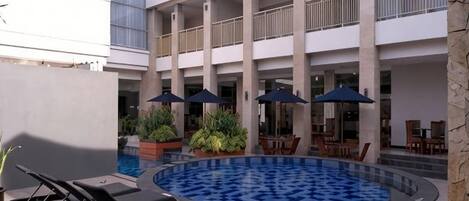 A hotel courtyard with a swimming pool, lounge chairs, and outdoor seating.