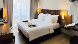 A hotel room with a large bed, a desk, a lamp, and a view of the city through the window. - Vrata Hotel Yogyakarta (Kalasan)