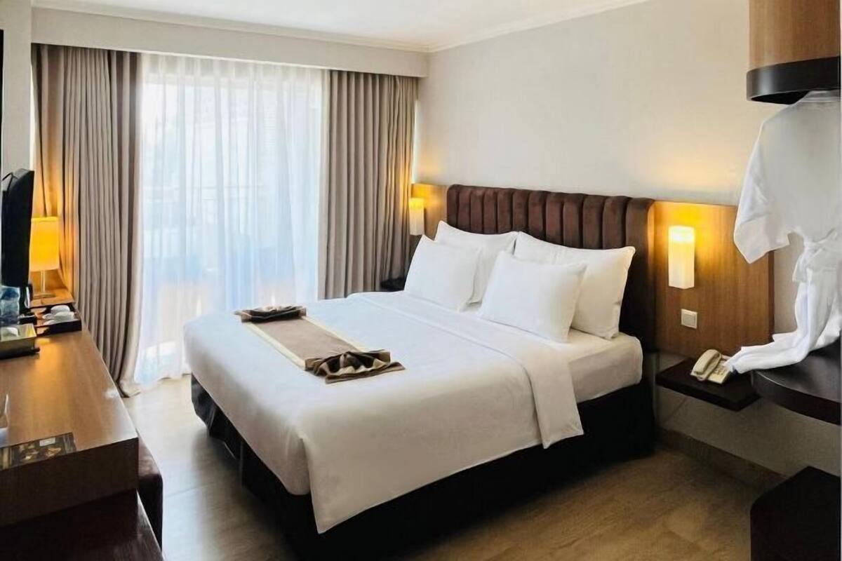 Une chambre d’hôtel avec un grand lit, un bureau, une lampe et une vue sur la ville par la fenêtre.