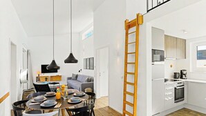 Une cuisine moderne avec des meubles blancs, une échelle en bois et un coin repas comprenant une table ronde et des chaises noires.